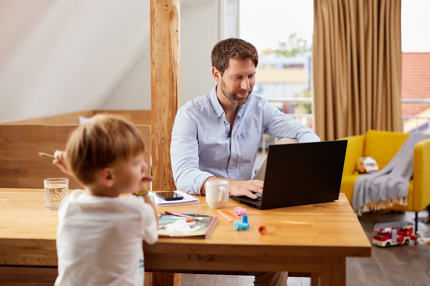 Ein Mann sitzt zuhause im Homeoffice an seinem Laptop. Bei ihm am Tisch spielen Kinder 