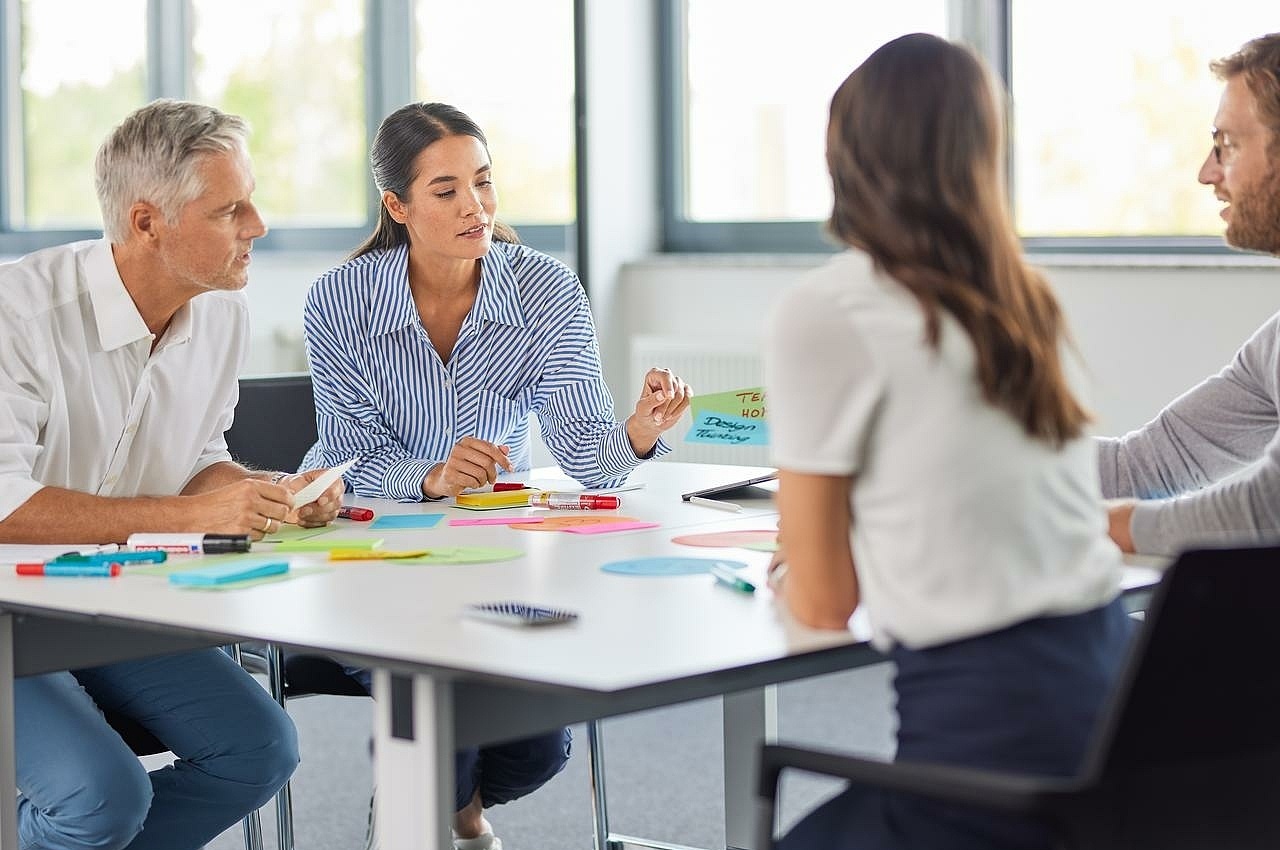 Eine Gruppe von Mitarbeitenden sitzt an einem Tisch und ordnet bunte Karten an