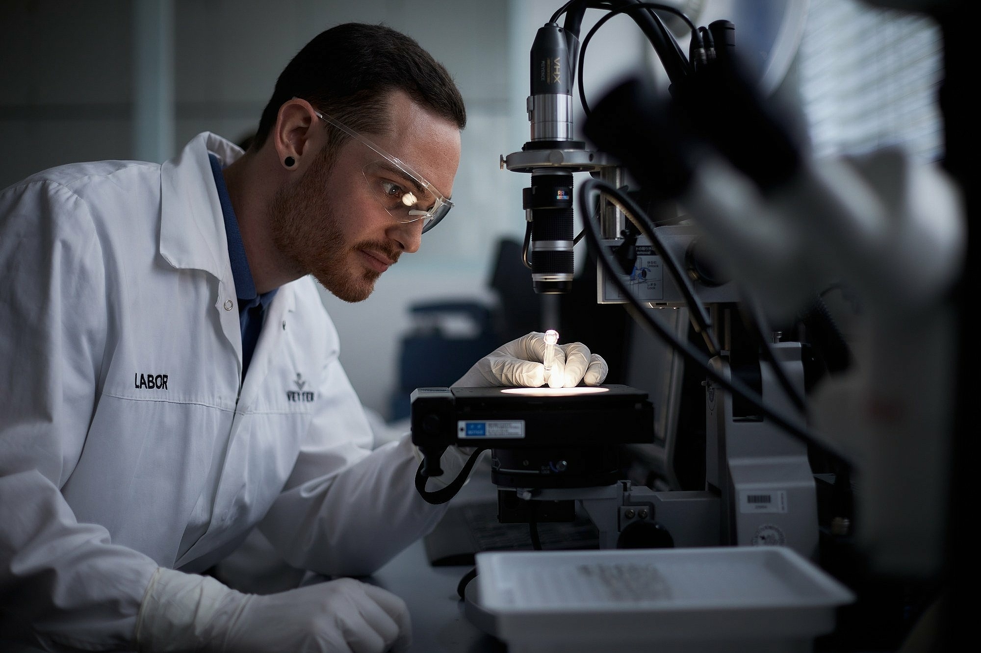 Ein Mitarbeiter in Laborkleidung arbeitet an einem Mikroskop im Labor 