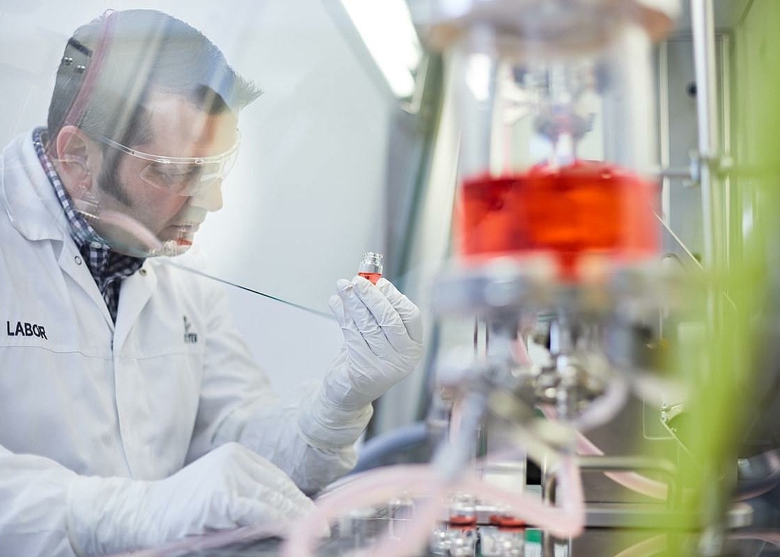 Ein Mitarbeiter arbeitet mit einer roten Flüssigkeit in Laborkleidung im Labor