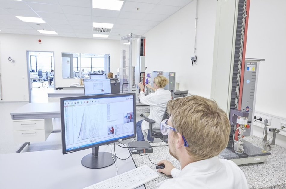 Mitarbeitende die eine Qualitätskontrolle in Laborkleidung am Computer im Labor durchführen 