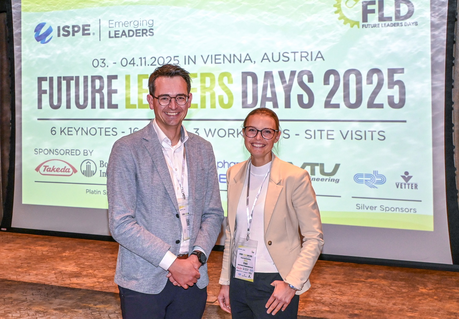Zwei Personen stehen vor einer großen Leinwand mit dem Schriftzug ‚Future Leaders Days 2025‘