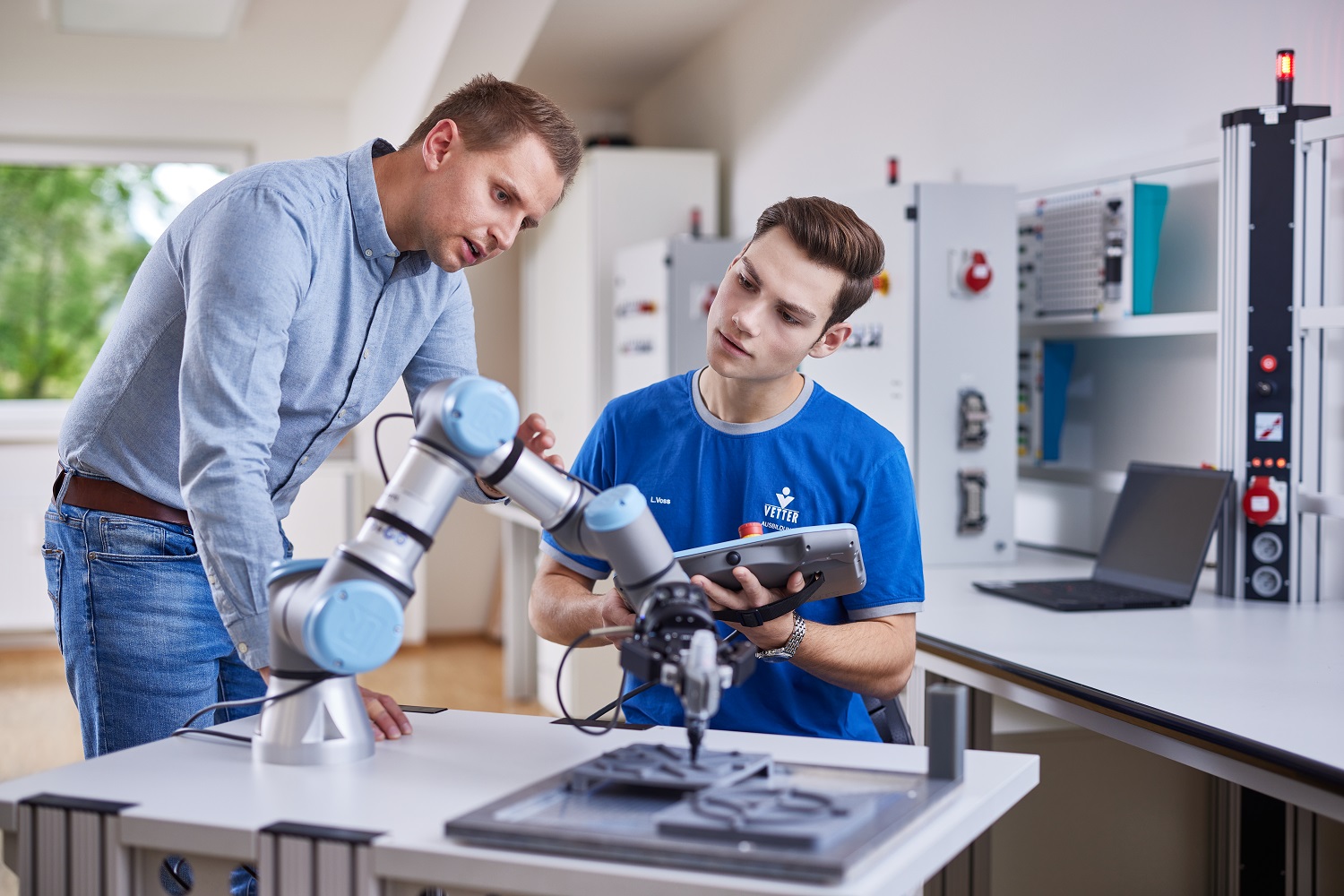 Ein Ausbilder zeigt einem Auszubildenden einen Roboter in der Mechatronik